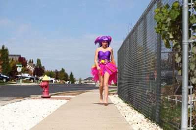 Young woman in costume while walking on sidewalk against sky