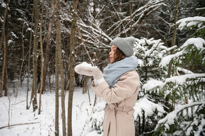 A cute girl in a hat and vazherzh holds snow in her hands and blows on it