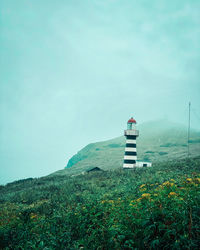 Lighthouse by building against sky