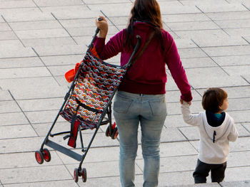 Rear view of mother with baby carriage and daughter walking on floor