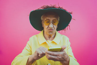 Close-up of senior woman using phone against pink background