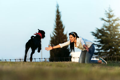 Woman playing with dog on field at park against sky