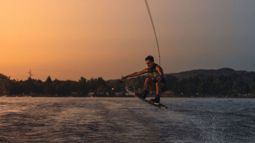 Rear view of man jumping in sea against sky during sunset