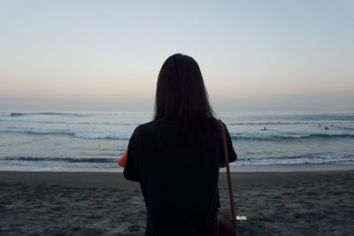 Rear view of woman standing on beach against clear sky