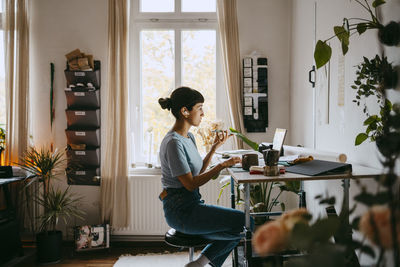 Side view of female business professional talking through speaker phone while sitting at home office