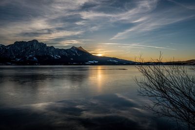 Scenic view of lake by snowcapped mountains against sky during sunset