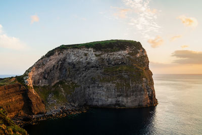 Rock formation by sea against sky during sunset