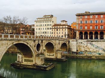 Arch bridge over river against buildings in city