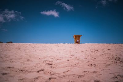 Lifeguard hut on sand at beach against blue sky