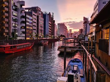 Canal amidst buildings in city against sky during sunset