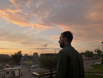 Man looking at cityscape against sky during sunset