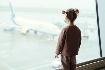 Child with backpack looking though airport window at the airplane. safe travels with kids during