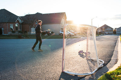 Teen boy playing street hockey alone on a residential street.