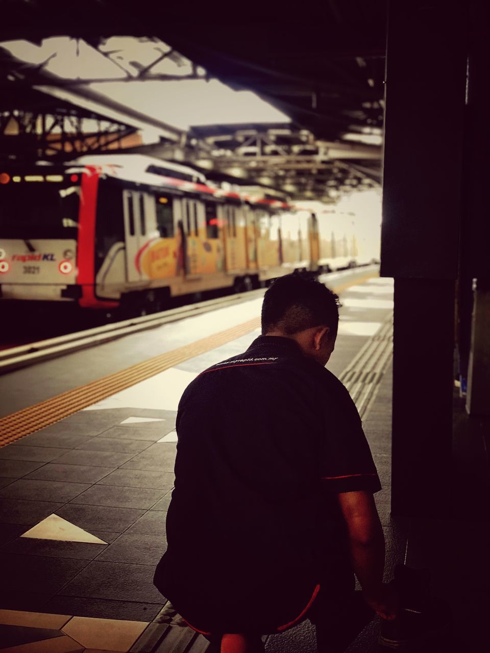 one person, rail transportation, transportation, public transportation, real people, men, railroad station, architecture, rear view, mode of transportation, standing, train, lifestyles, railroad station platform, built structure, three quarter length, train - vehicle, leisure activity, casual clothing, track, waiting