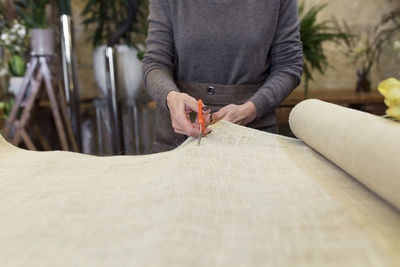 Cropped image of senior woman cutting fabric with scissors at desk