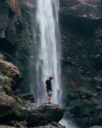 Man standing by waterfall on rock