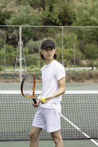 Front portrait of a young athletic tennis player and waiting to play on the green court.