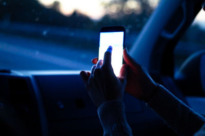 Cropped image of hands using mobile phone in car