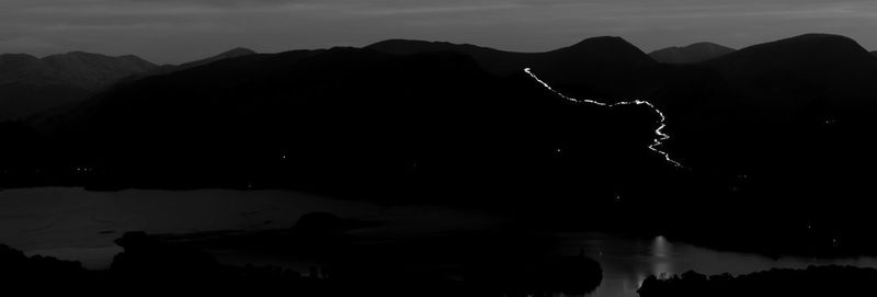 Silhouette mountain by lake against sky at night