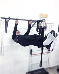 Full length of man hanging on bar in gym