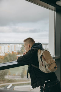 Side view of man looking through window against sky