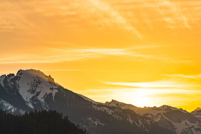 Scenic view of snowcapped mountains against orange sky