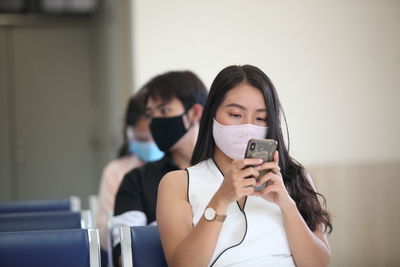 Woman wearing mask using mobile phone while sitting on chair