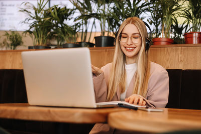 A smiling student wearing glasses and headphones works and studies online using wireless technology