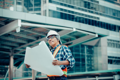 Manual worker with blueprint standing at construction site