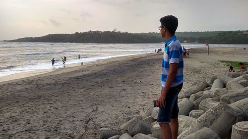 Full length of man sitting on rock at beach against sky