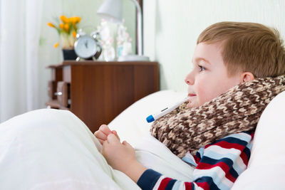 Cute boy holding thermometer in mouth at home