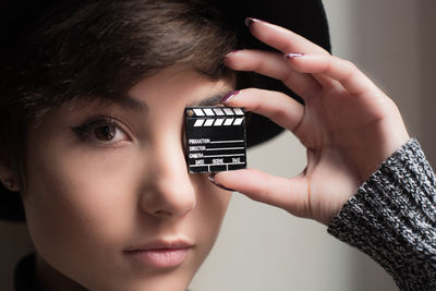 Close-up portrait of young woman covering eye with small film slate