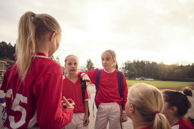 Girls wearing red soccer uniform talking against sky