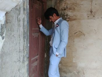 Side view of young man standing against wall