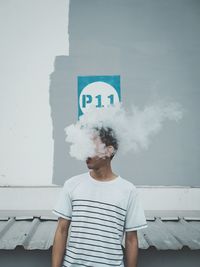 Young man smoking while standing against wall