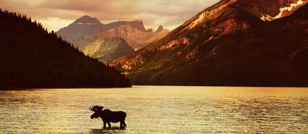 Silhouette mountain by lake against sky during sunset