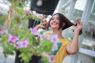 Young woman holding flowering plants while standing by potted plant