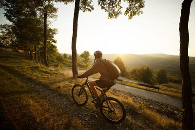 Male athlete cycling on footpath in field against clear sky