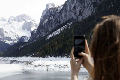 Woman photographing through smart phone on snow covered mountain