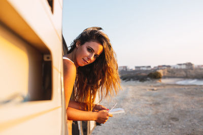 Portrait of young woman standing on smart phone against sky