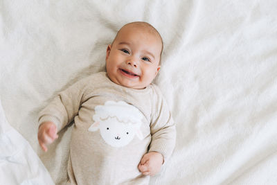 Cute smiling baby boy 4-6 month in beige overall on bed, natural tones