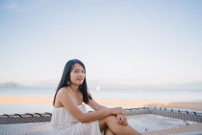 Young woman sitting in sea against sky
