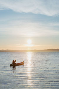 Man in canoe  against sky during sunrise