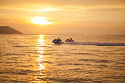 People riding jet boats sea against sky during sunset