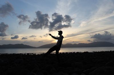 Silhouette man standing at beach against sky during sunset