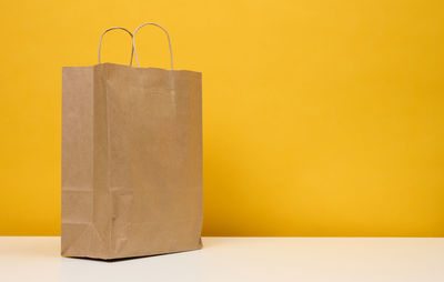 A brown paper bag stands on a white table, yellow background. product packaging, copy space