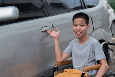 Portrait of smiling boy on wheelchair against car