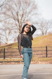 Young woman shielding eyes while standing on road in city