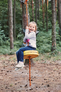 Portrait of happy girl playing on swing against trees