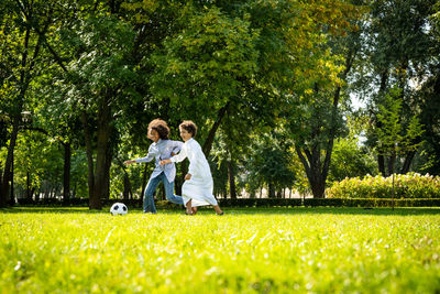 Rear view of couple walking on grassland against trees